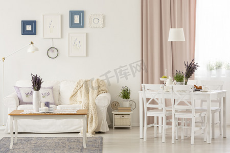 在白色客厅的桌子上的花朵, 粉红色的窗帘和海报以上的沙发上。真实照片