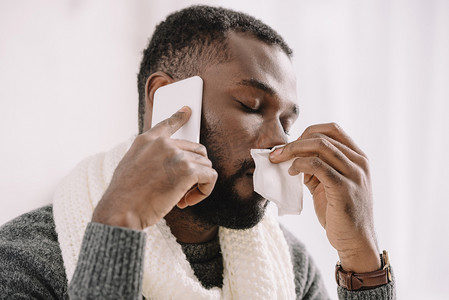 智能医疗设备摄影照片_生病的非洲裔美国男子与流鼻涕拿餐巾, 而在智能手机上交谈