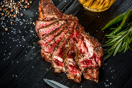 自助烧烤摄影照片_烧烤干岁的肋的牛肉、 香料、 蔬菜以及一杯淡啤酒特写黑色木制背景