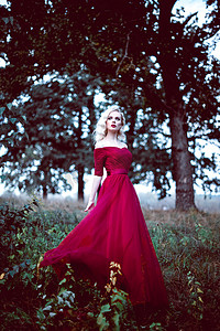 时尚华丽年轻的金发女郎在漂亮的红色裙子，在一个童话般的森林。魔幻的气氛。被修饰调色射击