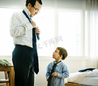 father teaching boy to put on tie.