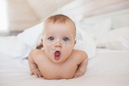 表情装饰惊讶摄影照片_肖像的小宝宝躺在白色的床上，打开她的嘴