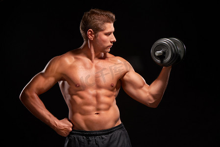 Shirtless sexy muscular sportsman pumping up biceps with black dumbbell