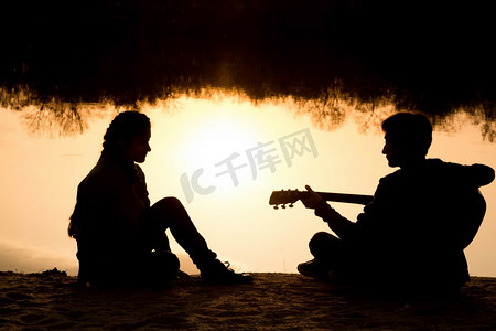 江上风景摄影照片_一个年轻的男孩和女孩在沙滩上用一把吉他的剪影