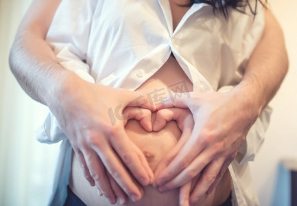 产妇的概念与幸福的夫妇手牵着手，在大肚子，在孕妇的肚子上创建一颗心