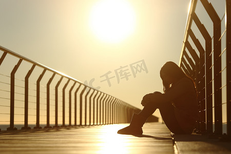 悲伤的十几岁的女孩沮丧在日落时分坐在一座桥