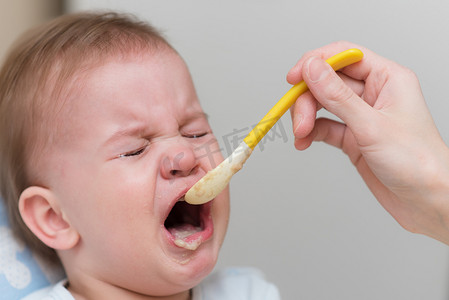 喊叫声摄影照片_婴儿哭了，不肯吃蔬菜泥