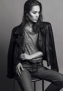 时尚fashion摄影照片_Portrait of a fashionable model with natural make up and perfect skin, dressed in men's jeans, grey shirt, black jacket and sneakers.  Studio shot. High fashion look. Monochrome (black and white)  photo