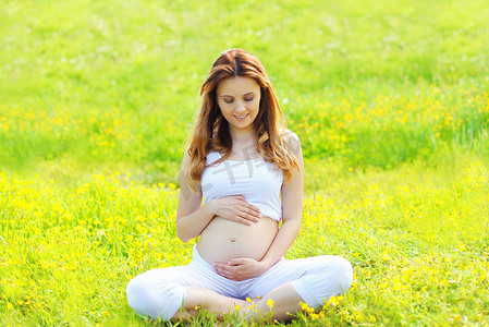 幸福的怀孕女人坐在做健身或瑜伽的草地上 