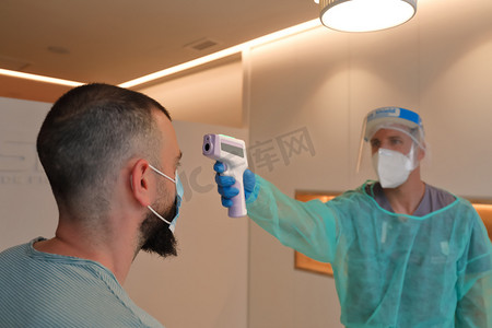 男性医务工作者佩戴防护面罩，用数字无接触式温度计测量病人体温