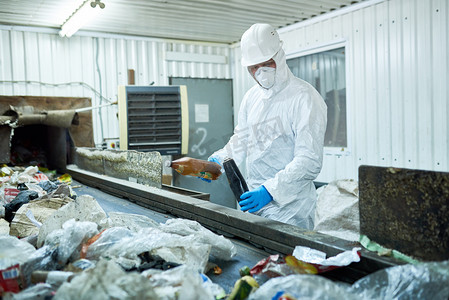 工人穿着生物危害服和安全帽工作在废物处理厂的肖像输送带可回收材料的分类