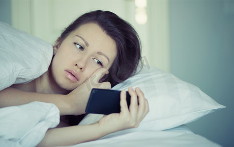 一个漂亮的女孩躺在床上，不能入睡并读取在智能手机上的新闻。失眠。心理学。恐惧症