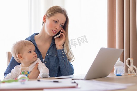 忙着呢摄影照片_工作母亲与婴儿在她腿上，在家工作