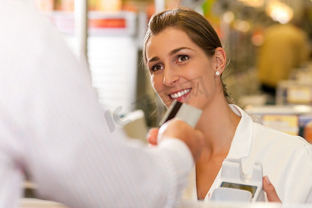 超市里的一名男性顾客把信用卡交给收银台的收银员，以便付款
