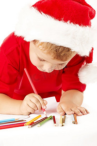 圣诞老人帽子摄影照片_戴着圣诞老人帽子的小男孩在床单上画画