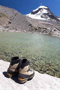 日是背景摄影照片_徒步旅行靴，背景，背景是湖泊和积雪的山峰(意大利Gran Paradiso国家公园)。