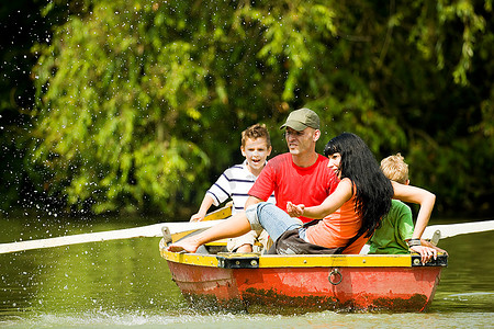 一家人带着两个孩子在湖上划船旅行，背景是许多树木和鲜花