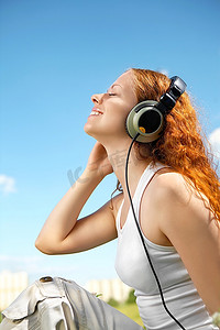 女孩的侧影，在天空的映衬下，在大耳机里享受音乐
