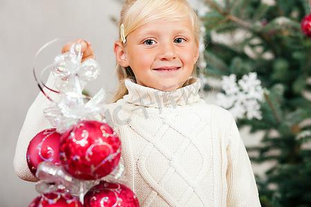 年轻女孩手持圣诞小玩意儿，帮忙装点圣诞树。