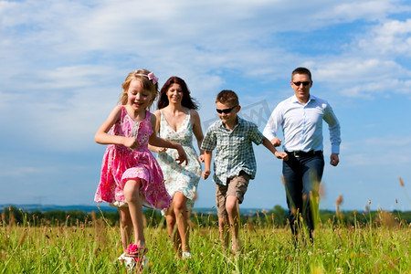 快乐的家庭-母亲、父亲、孩子-在踢足球的夏天跑过一片绿色草地