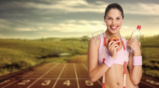 一位年轻的女运动员拿着水和苹果与跑道对抗。