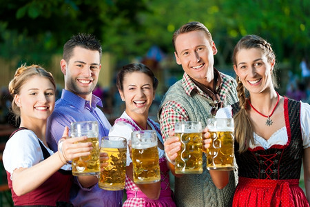 在啤酒花园-朋友在Tracht，Dirndl和Lederhosen喝新鲜的啤酒在巴伐利亚州，德国