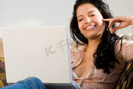 一位年轻漂亮的西班牙裔妇女坐在沙发上玩着她的笔记本电脑