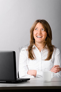 一位女商人拿着笔记本电脑坐在办公室里，若有所思地斜视着。