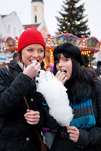 圣诞集市上的两个女人在摊位前吃棉花糖，天气很冷