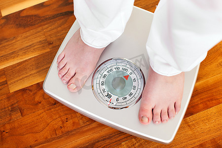 女人(只能看到她的脚)站在浴室秤上测量体重，控制她的节食结果