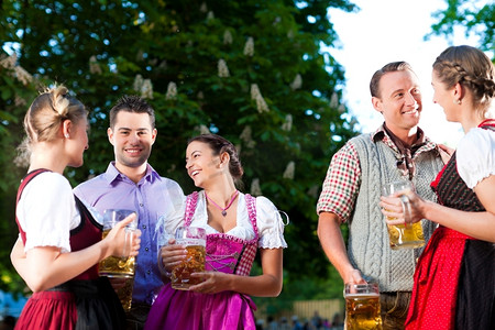 在啤酒花园--在特拉赫特的朋友，迪恩德尔和莱德霍森在德国巴伐利亚州喝着新鲜啤酒聊天