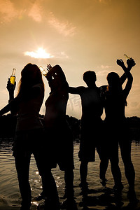 朋友聚会剪影摄影照片_海滩上的人们(两对)随着音乐跳舞，喝酒，在夕阳下只能看到的人群的剪影中玩得很开心