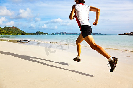 一个年轻人在日出时分在热带空旷的海滩上奔跑；塞舌尔，印度洋