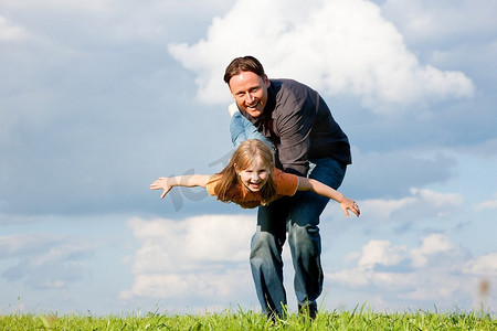 父亲和他的儿女一起在草地上玩耍，他用手抱着她
