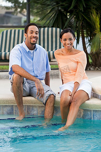 一对幸福的三十多岁的非裔美国夫妇在游泳池里用脚坐着