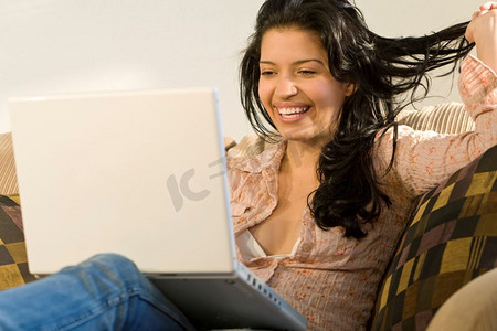 一位年轻漂亮的西班牙裔妇女一边用笔记本电脑一边笑着