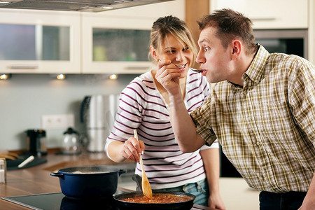 一对夫妇在他们的厨房里一起做饭，品尝酱汁的人发现它非常辣--你可以从他的面部表情看出