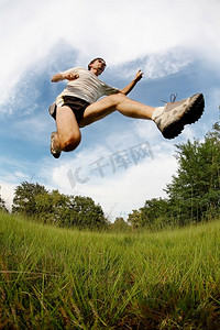 男性跑步者在蓝天和云朵的映衬下在草地上跳跃和奔跑；模糊效果，鱼眼镜头。复制-底部的空格。
