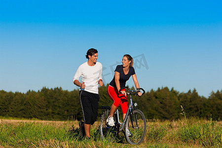 在晴朗的蓝天下，年轻的健身夫妇在秋天进行户外运动、慢跑和骑自行车