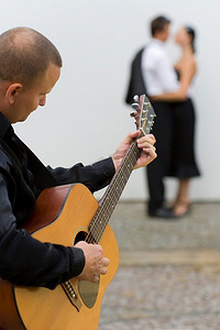 一个街头音乐家弹着吉他为两个年轻的恋人唱小夜曲