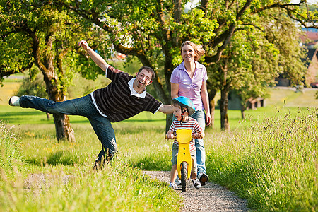 儿童大自然摄影照片_一家人夏天在户外散步，他们的小儿子骑着训练自行车，未受破坏的大自然