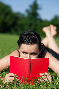 夏天教育摄影照片_夏天躺在草地上晒太阳看书的女人，焦点放在书上