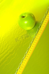 绿色的苹果放在金色的背景上，上面有卷尺和链子