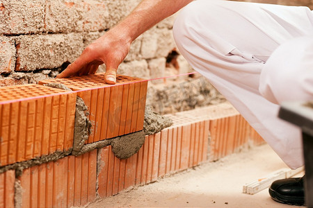瓦匠在铺砖筑墙，他用铲子从一个接缝里拔出灌浆。这个男人真的很努力。