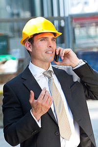 一名戴着黄色安全帽、身穿西装的男子在工业或建筑工地上打手机
