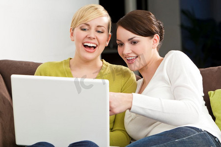 开心大笑的女人摄影照片_两个年轻漂亮的女人在白色笔记本电脑上玩得很开心