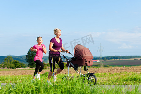 婴儿推车摄影照片_家庭运动--在阳光明媚的日子里，母女俩推着婴儿推车沿着小路慢跑