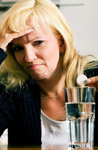 入杯摄影照片_患有严重偏头痛的妇女将止痛片放入一杯水中