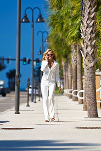 一位年轻漂亮的金发女子在电话里走在一条长满棕榈树的街道上。