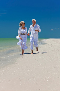 幸福的老年男女夫妇在晴朗蓝天的荒凉热带海滩上奔跑、欢笑、牵手